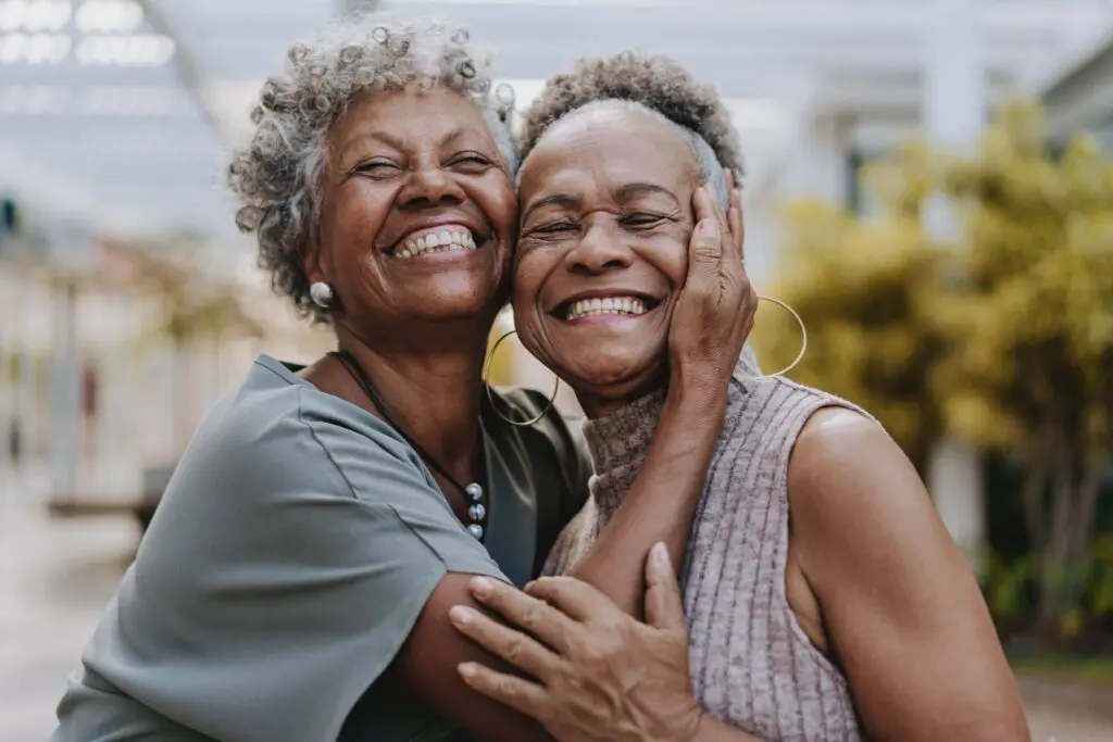 Two elderly black woman smiling and hugging for having joined the senior living waitlist at Kendal on Hudson in Sleepy Hollow, NY.