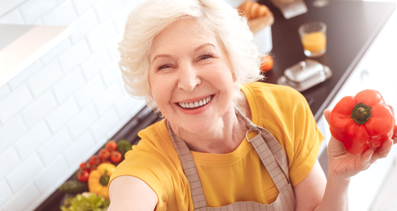 Woman in the kitchen smiling and holding a red pepper