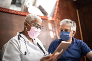 A female doctor wearing a mask next to a senior man wearing a mask