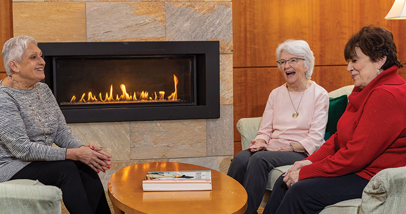 three seniors sitting by a fireplace