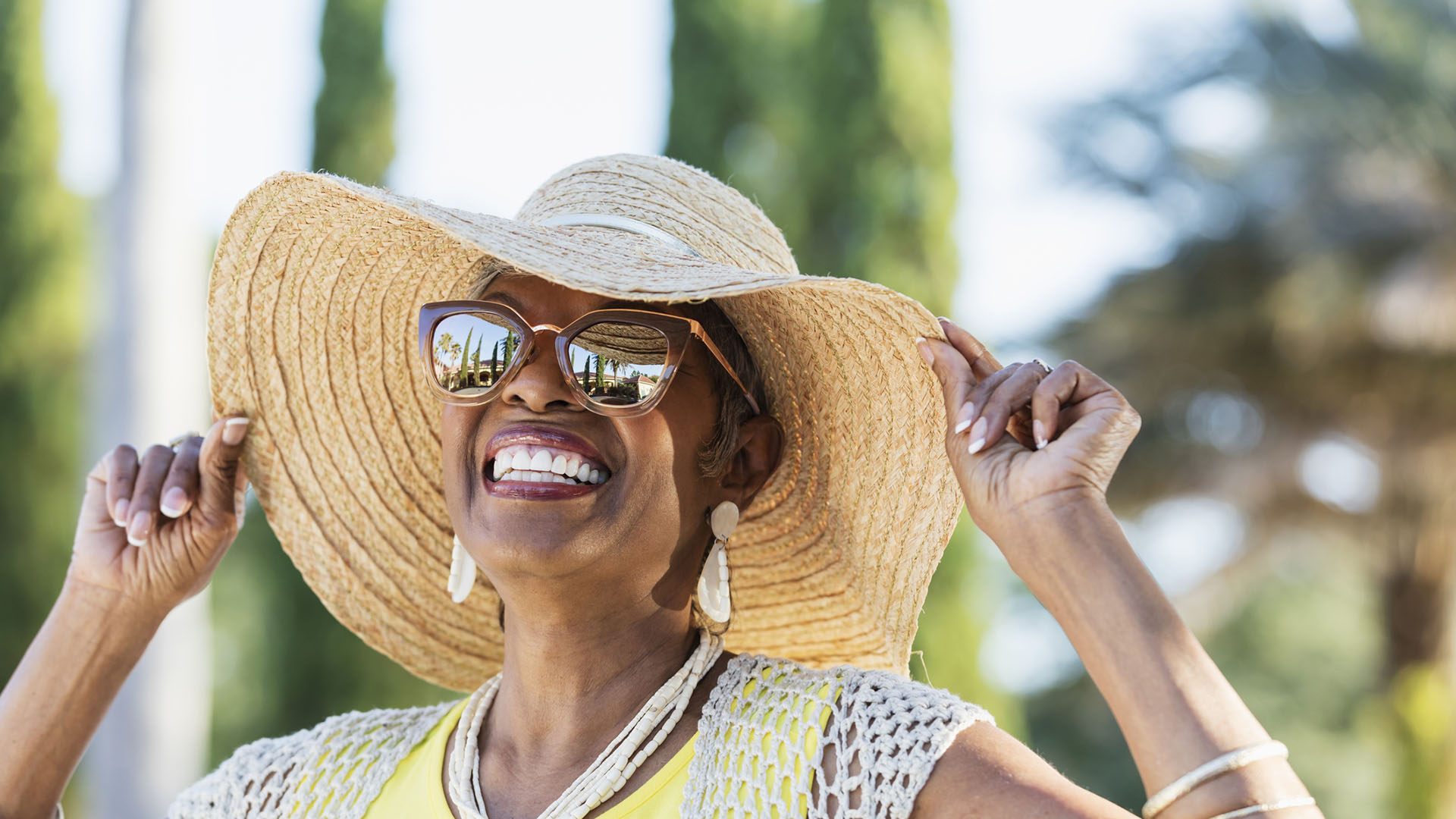 senior woman smiling outside in the summer following summer safety tips for seniors with a hat and sunglasses