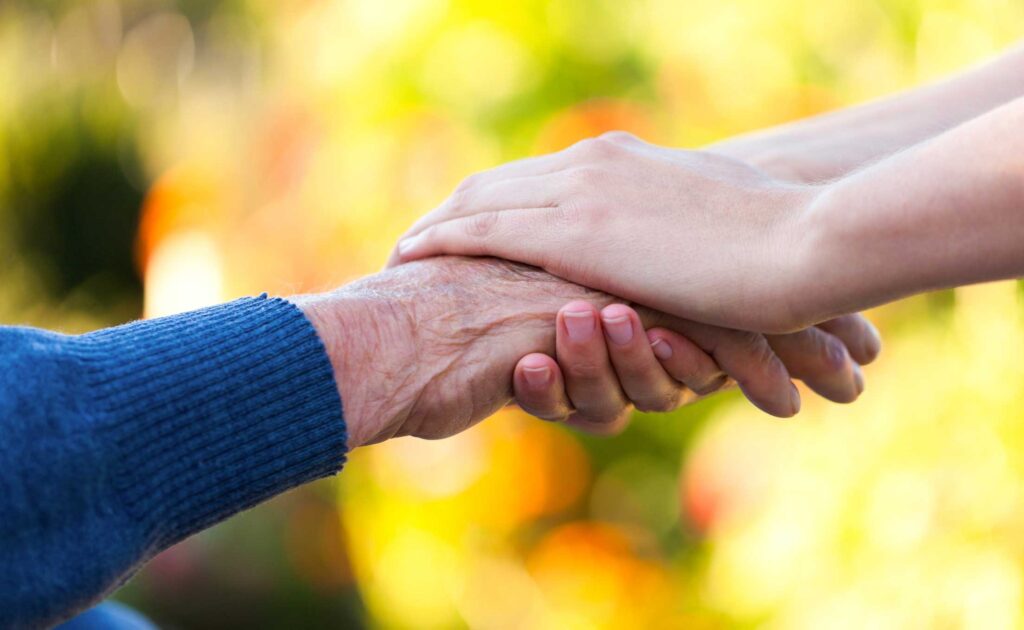 close up of a caregiver holding a senior man's hand