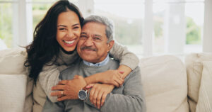 portrait of senior man with daughter, hugging on sofa in living room of home