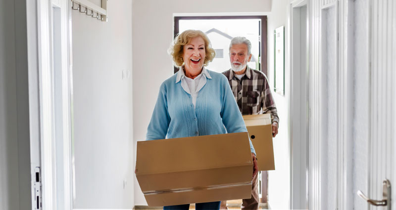 Senior couple moving boxes entering into new home, transitioning to a life plan community Sleepy Hollow, NY.