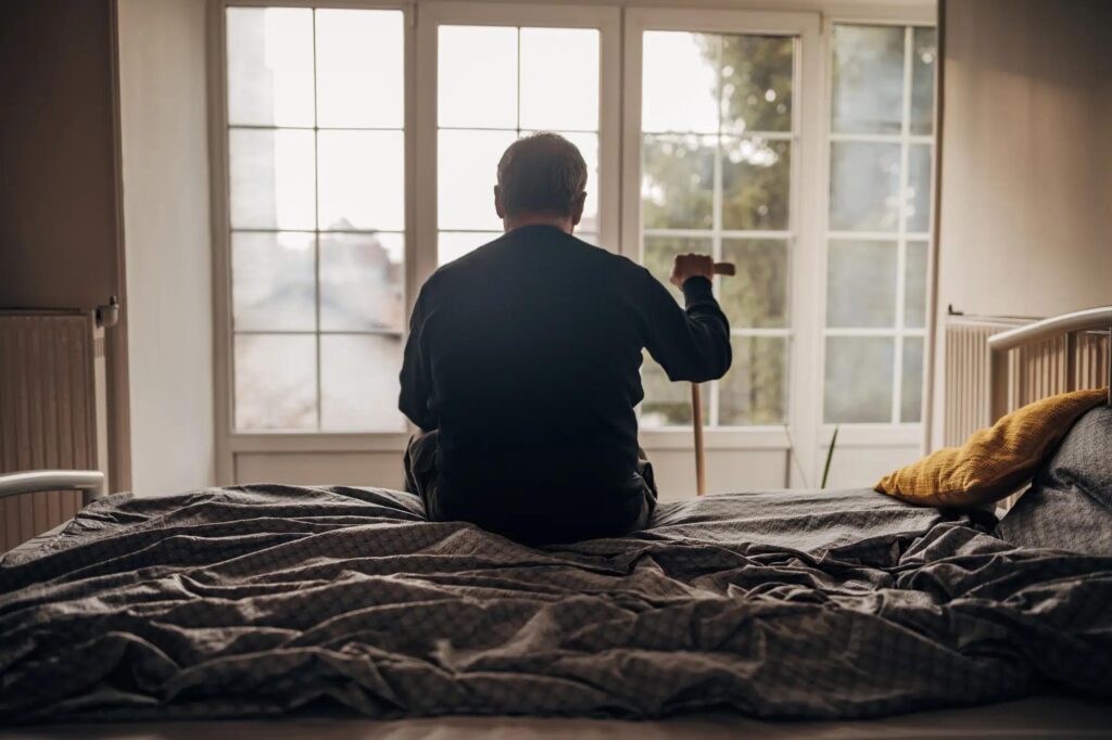 senior man sitting on bed facing window 