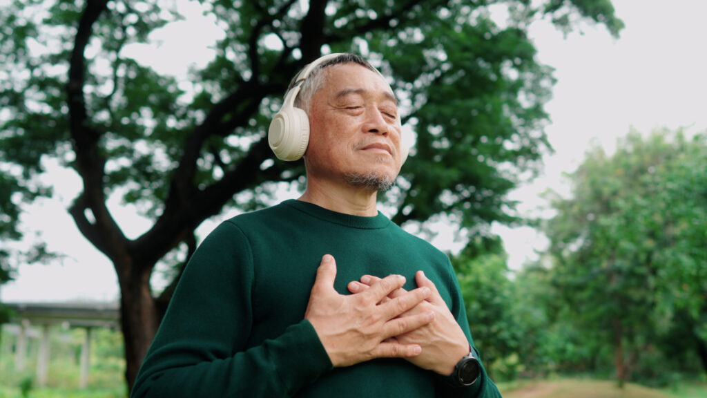 Elderly man meditating under a tree with wireless headphones